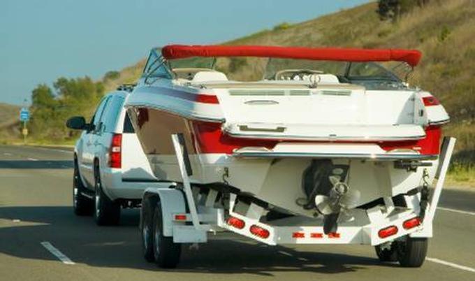White vehicle hauling a boat on a trailer.