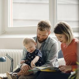 Parents holding their child while looking at a book.