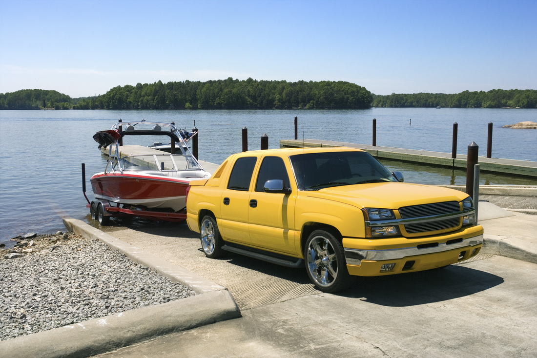 Yellow pickup truck backing red power boat on trailer into lake. 
