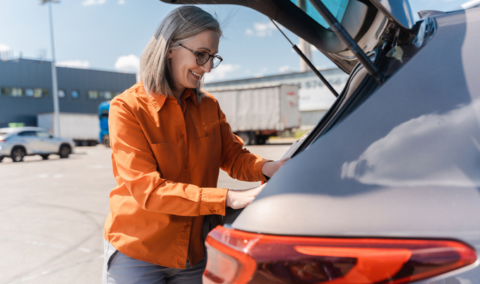 Smiling senior woman opening car trunk, searching something planning road trip. Transportation concept