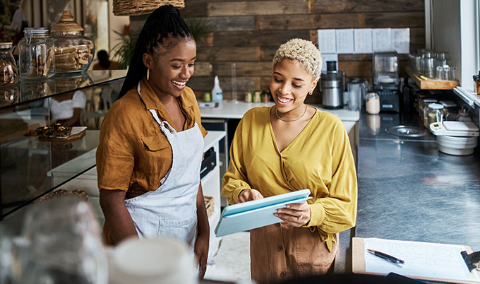 A cook and manager standing in a commercial kitchen looking at a tablet smiling.