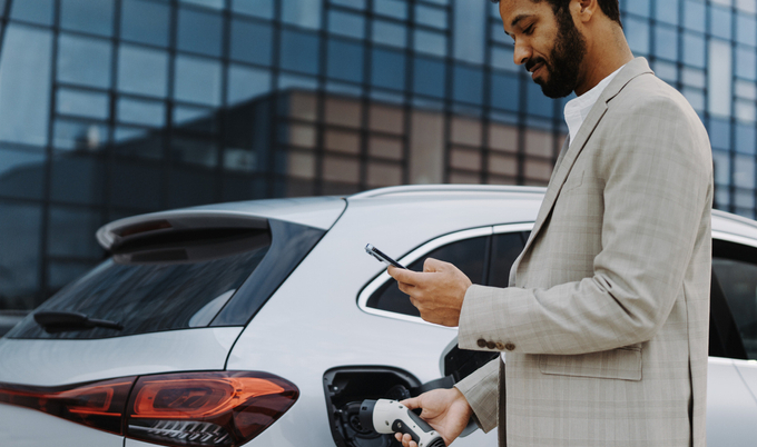 Man charging an electric vehicle (EV) while using his phone.