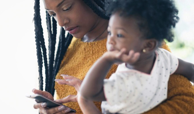 Mother holding toddler and using smartphone.