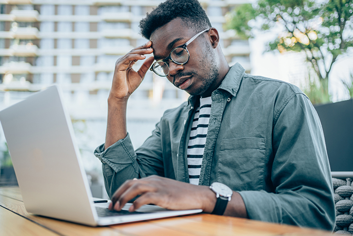 Stressed businessman using laptop at sidewalk cafe
