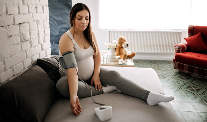 Pregnant woman checking blood pressure while sitting on the floor.