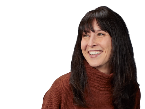 photo of a Caucasian woman wearing a brown sweater and jeans smiling with her hands behind her back