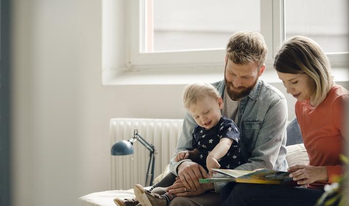 Parents holding their child while looking at a book.
