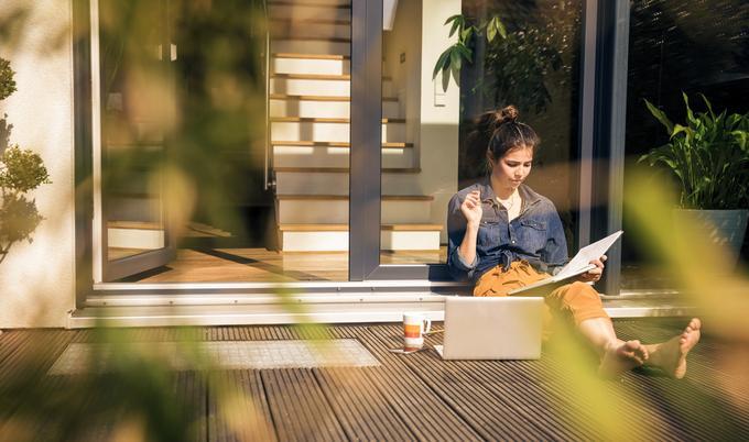 Young woman sitting on terrace at home working with book and laptop 