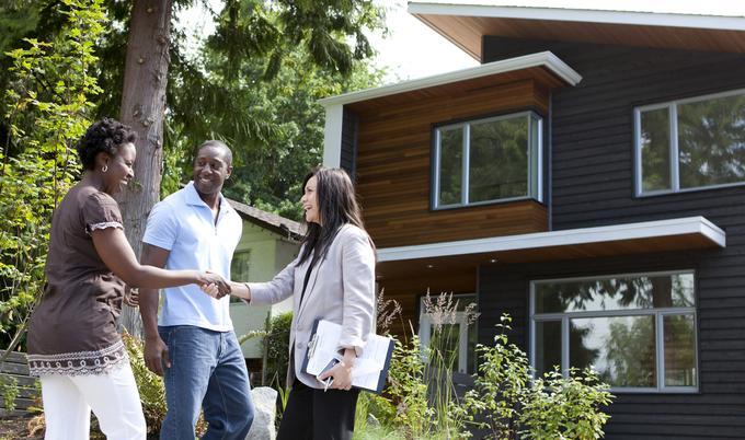 Real estate agent greeting couple outside house. 