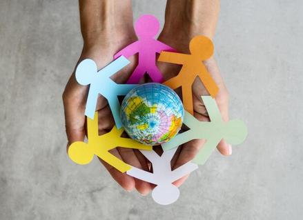 An out-reach open palm holding paper people surrounding a globe toy.