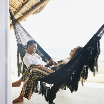 Smiling couple holding hands in hammock.