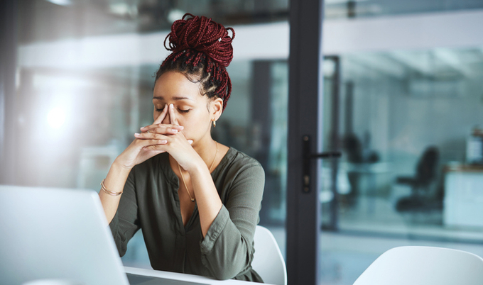 Woman sitting in front of a computer holding her hands to her face in frustration.