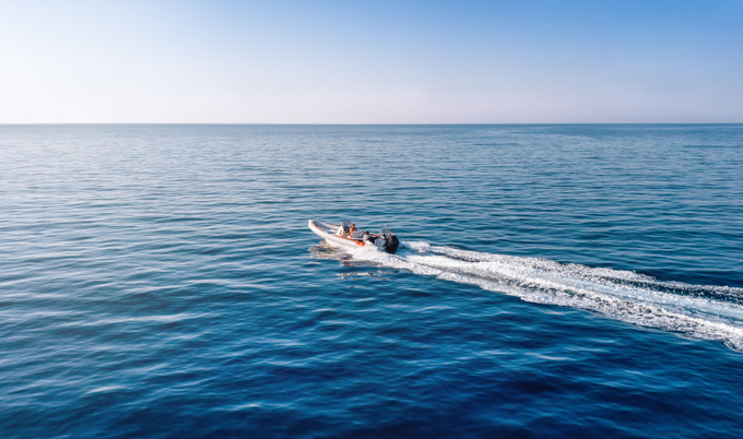 A speedboat cruises across calm blue ocean waters leaving white wake trails behind.