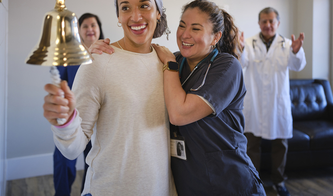 A woman celebrating her chemotherapy treatment with a ceremonial bell ring