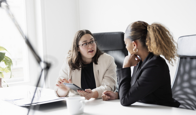 Two female professionals having a discussion in an office setting.