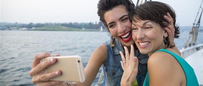 Two women take an engagement selfie on a sailboat.