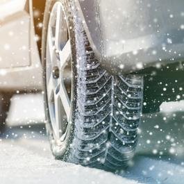 Close-up shot of a car's rear tire in snow while snowing. 