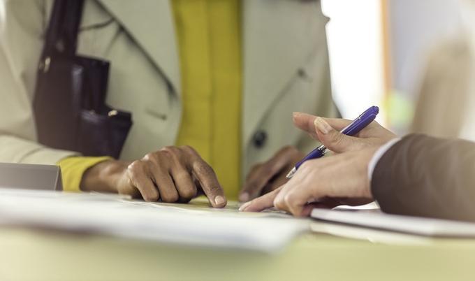 Two people standing at a service counter are discussing paperwork.