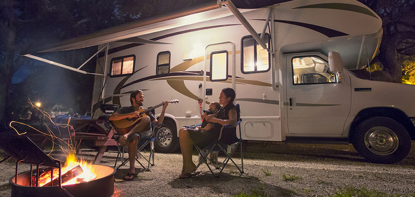 Family sitting in front of campfire and motor home at night