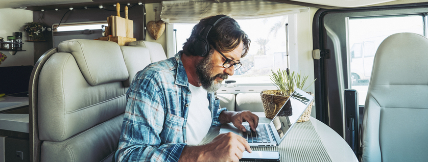 man working on mobile cell phone and laptop computer inside a camper