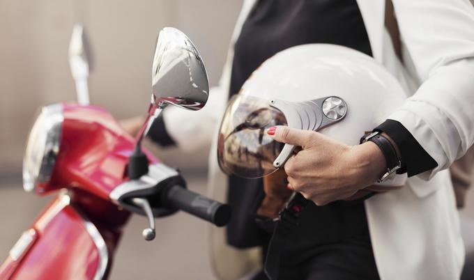 Woman holding a helmet next to a scooter.