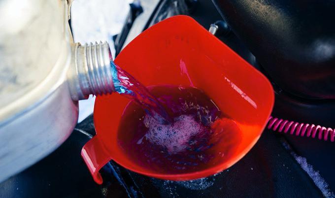 Pouring blue liquid into a funnel over an engine.