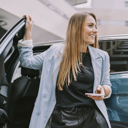Smiling woman with phone next to open car door