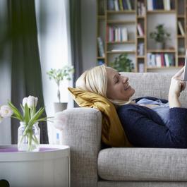 Woman lying on couch and using a tablet device.