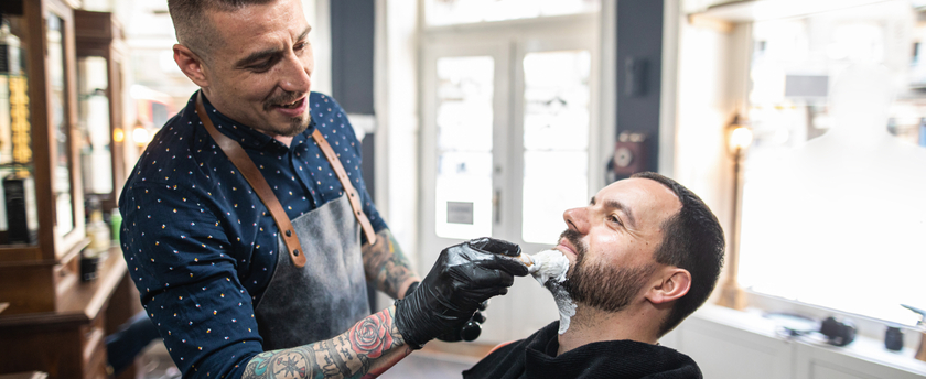 Skilled barber serving a customer at a vintage looking barber shop on a sunny day.