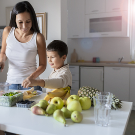 Mother and young boy cutting up fruits and vegetables in their kitchen