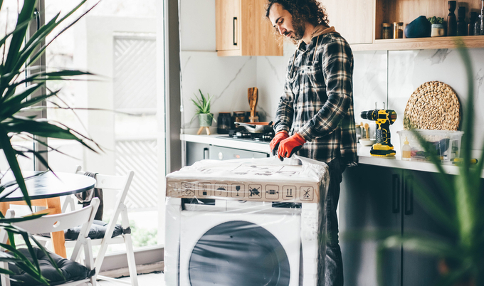 A man unwrapping a new washing machine to install in a home.