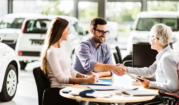 Man shaking hands with salesperson at car dealership. 