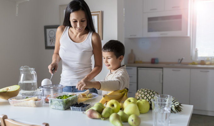 Mother and young boy cutting up fruits and vegetables in their kitchen