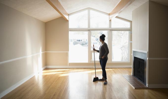Woman holding broom looks out window of new home.