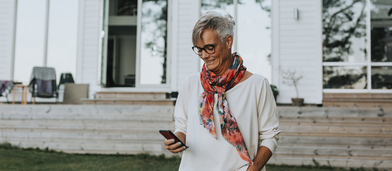 Smiling woman using cell phone in front of a house wearing a colorful scarf.