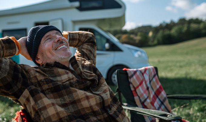 Man relaxing in a chair in a grassy field in front of their RV.
