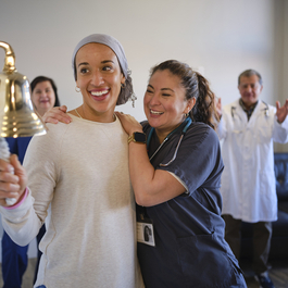 A woman celebrating her chemotherapy treatment with a ceremonial bell ring
