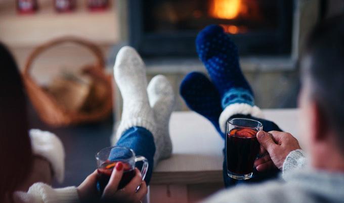 Mature couple with hot drinks in living room in front of fireplace.