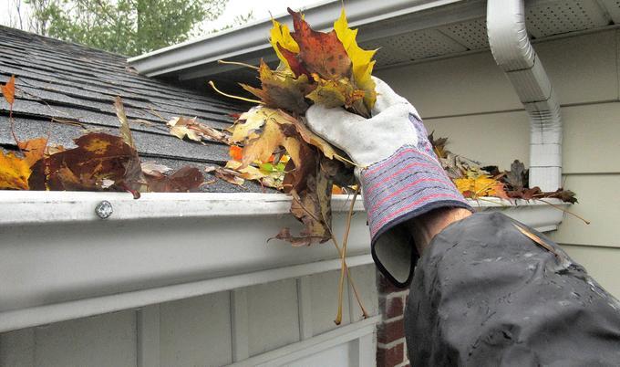 Gloved hand cleaning leaves of gutters.