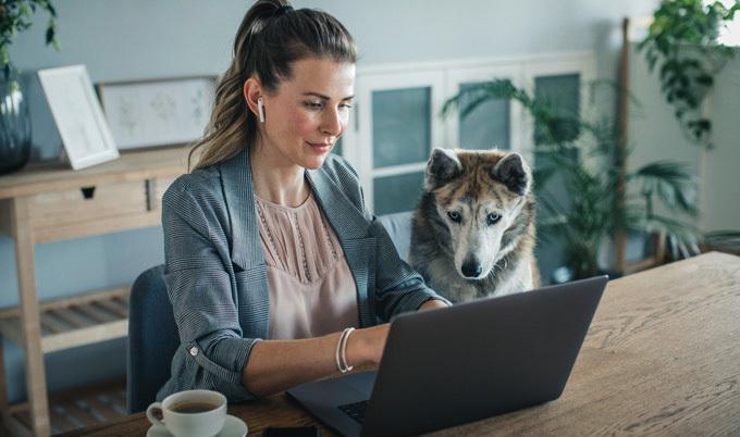 Woman wearing headphones working on her laptop with her dog on the side