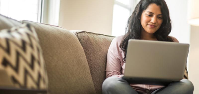 Woman sits on a couch with her legs crossed and types away on her laptop