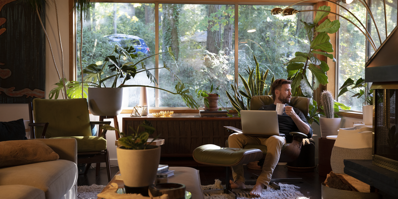 man lounging at home, on computer and drinking coffee