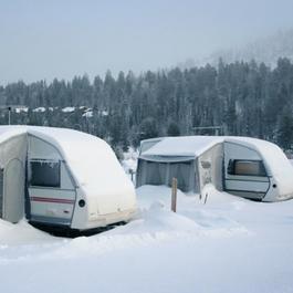 Light blue RV covered in snow in front of trees.