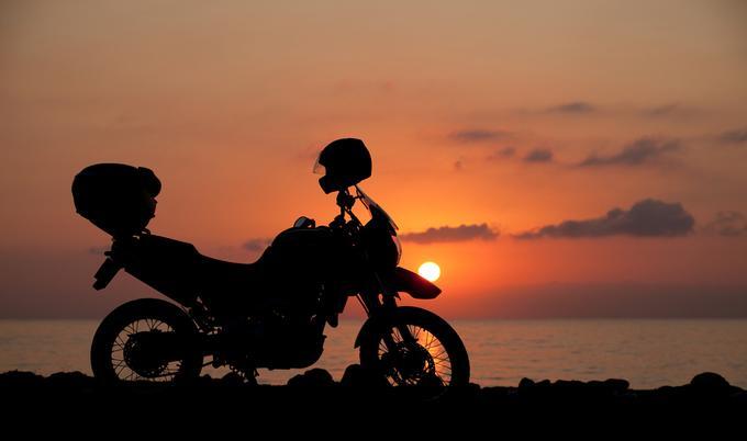 Motorcycle parked on beach at sunset.  