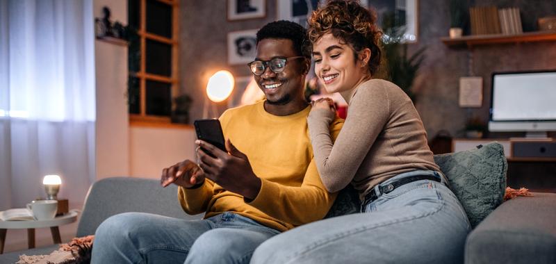 couple sitting on couch looking together at a cell phone