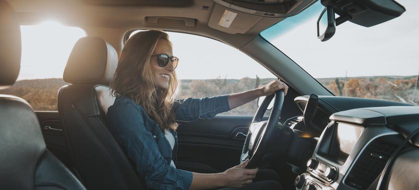 Inside view of a car, a woman is driving with sunglasses on as she looks down at the infotainment system.