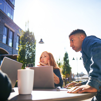 Three professionals collaborating on laptops outdoors next to an office building.