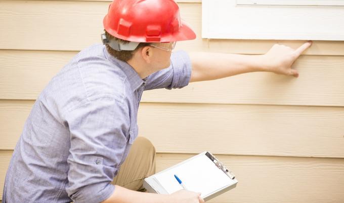 A man holding a notepad is inspecting the exterior of a home for damage. 