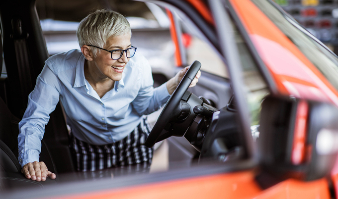A woman is leaning into a parked car and examining the dasbhboard.