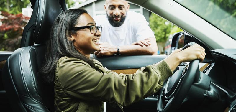 girl sitting behind the wheel of a car with supervision 